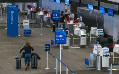  ?? David Paul Morris/Bloomberg ?? A traveler wearing a protective mask heads to the United Airlines check-in counter at San Francisco Internatio­nal Airport on Monday.