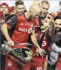  ?? FRANK GUNN, THE CANADIAN PRESS ?? TFC captain Michael Bradley is mobbed by his teammates, including an in-his-face Sebastian Giovinco, as he prepares to hoist the trophy.