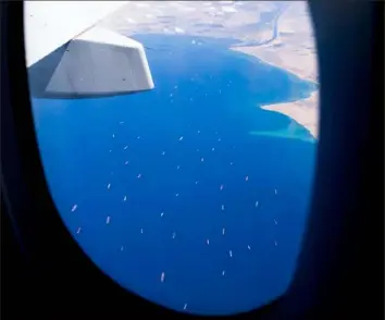  ?? Mahmoud Khaled/AFP via Getty Images ?? Seen from the porthole of a commercial plane Saturday, stranded ships wait in queue in the Gulf of Suez to cross the Suez Canal at its southern entrance near the Red Sea port city of Suez. The waterway remains blocked by a container ship.