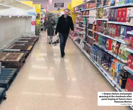  ?? Jonathan Myers ?? > Empty shelves and people queuing at the checkouts after panic buying at Tesco’s store Swansea Marina