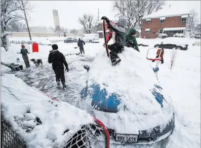  ?? Steve Griffin The Associated Press ?? Katie and James Thomas, back, dig out from a snowstorm that dumped several inches of snow as their children make a sledding hill out of their car Wednesday in Salt Lake City.