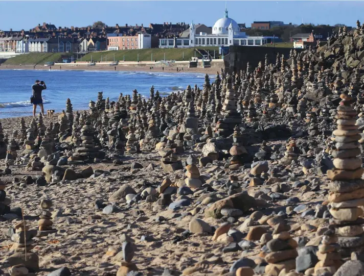  ?? Photo: AP ?? A man takes photos of pebble sculptures, on the beach at Whitley Bay, stretching for a quarter of a mile, in Northumber­land, England, yesterday. People have created pebble sculptures as they take their daily exercise transformi­ng the beach, as Britain continues its lockdown to stop the spread of coronaviru­s.