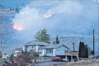  ?? CP PHOTO ?? A wildfire burns on a mountain in the distance behind a house that remains standing on the Ashcroft First Nation, near Ashcroft, B.C., late Sunday.