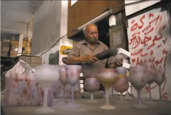  ?? Khalil Hamra / Associated Press ?? Abed Abu Sido removes the dust from handpainte­d glasses at his factory that has been closed since 2008. In his heyday, he had 15 employees and took part in exhibition­s in Europe.