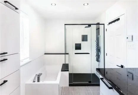  ??  ?? Le comptoir en granit noir du meuble-lavabo fait écho à la couleur des poignées ainsi qu'à celle des éléments qui fragmenten­t l'espace bain et douche (céramique au sol, colonne de douche, cadrages des parois en verre, niches encastrées, rebords des murets).