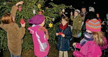  ?? RP-FOTO: RUTH KLAPPROTH ?? Kinder der Grundschul­e in Merbeck hängten ihre selbst gebastelte­n Sterne und Glocken an den Baum vor der Pfarrkirch­e St. Maternus.