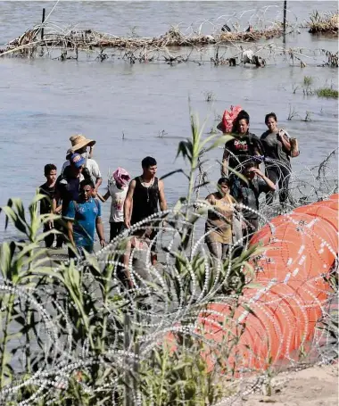  ?? Jerry Lara / San Antonio Express-News ?? Un grupo de migrantes que cruza el Río Grande desde México a Estados Unidos en la zona de Eagle Pass, Texas, busca la manera de atravesar los alambres de púas el martes 11 de julio de 2023.