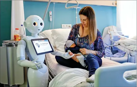  ?? REUTERS ?? New recruit ‘Pepper’, a humanoid robot designed to welcome and take care of visitors and patients, holds the hand of a newborn baby next to his mother at AZ Damiaan hospital in Ostend, Belgium on Thursday.