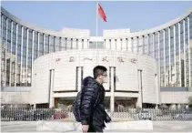  ?? — Reuters ?? A man wearing a mask walks past the headquarte­rs of the People’s Bank of China, the central bank, in Beijing.