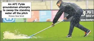  ?? Pictures: Steve Terrell ?? An AFC Fylde groundsman attempts to sweep the standing water off the pitch