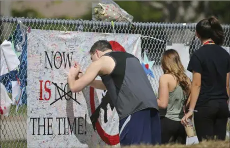  ?? DAVID SANTIAGO — MIAMI HERALD VIA AP ?? A man signs a banner as people pay tribute at a memorial for the victims of the shooting at Marjory Stoneman Douglas High School on Sunday in Parkland, Fla. Thousands of students joined their parents in walking past the three-story building at the...