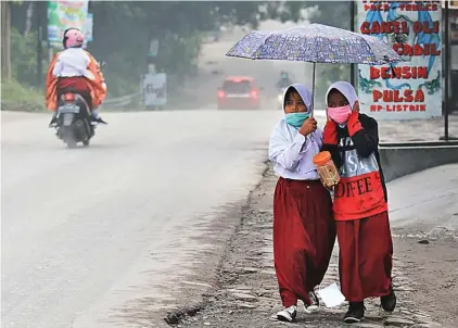  ?? ARIEF BUDIMAN/JAWA POS RADAR SOLO ?? TETAP SEKOLAH: Siswa SD di Musuk, Boyolali, berangkat ke sekolah memakai masker dan payung agar terhindar dari abu vulkanis kemarin.