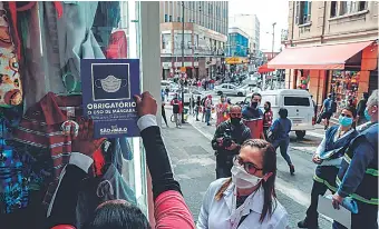  ??  ?? Personal de la Vigilancia Sanitaria fiscaliza un comercio y el uso obligatori­o de mascarilla­s en el centro de São Paulo, Brasil.