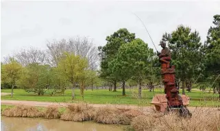  ?? John DeLapp / Correspond­ent ?? Chainsaw artist James Phillips’ sculpture of a boy fishing stands beside a pond at Taylor Lake Village Community Park. Another sculpture in the park depicts a NASA rocket.