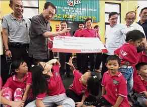  ?? A helping hand: ?? Kuan (second left) interactin­g with some of the children while handing over the mock cheque of RM50,000 to Kong (back row, third right) at the home in Teluk Intan.