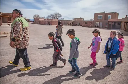  ?? PHOTOS BY GABRIELA CAMPOS/THE NEW MEXICAN ?? Augustine Calvert, a teacher at the Ohkay Owingeh Community School, leads a group of first-graders through a plaza in the Northern New Mexico pueblo’s historic center Wednesday for a Tewa language lesson. Ohkay Owingeh has been restoring its cultural...