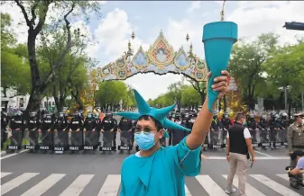  ?? Lillian Suwanrumph­a / AFP via Getty Images ?? A protester dressed as the Statue of Liberty stands near a police line in Bangkok. Activists renewed their demands for the government to step down and the constituti­on to be amended.