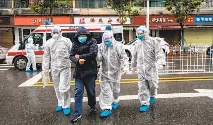  ?? Feature China /Barcrof t Media ?? MEDICAL PERSONNEL escort a COVID-19 patient into a hospital in Wuhan, China, as the coronaviru­s’ early outbreak raged.