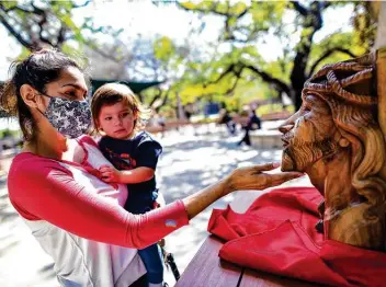  ?? Photos by Billy Calzada / Staff photograph­er ?? Mary Sanchez holds her son, Nehemiah, as she touches a wood carving of the face of Jesus Christ at Our Lady of Lourdes Grotto, where about 150 faithful took part in the Stations of the Cross tradition.