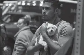  ?? SHABAN ATHUMAN/DALLAS MORNING NEWS ?? Isaiah Allen, a resident of the damaged Elan City Lights apartments, holds onto a dog, Princess, as he watches officials respond to a scene after a crane collapsed into the apartments in Dallas on Sunday. Allen was in his apartment when he said he heard what he thought was the loudest thundercla­p he had ever heard, but quickly realized the sound came from the collapsed crane.