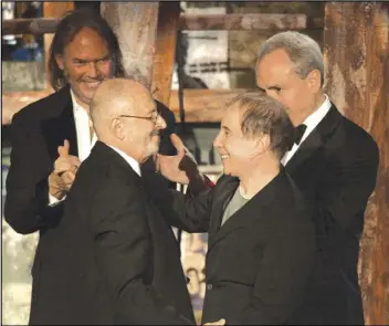  ?? GREGORY BULL/AP PHOTO ?? Record executive Mo Ostin (foreground left) is embraced by singer/songwriter Paul Simon (right) as singer/songwriter Neil Young (background left) and producer Lorne Michaels look on after Ostin was inducted into the Rock and Roll Hall of Fame in New York, in 2003.