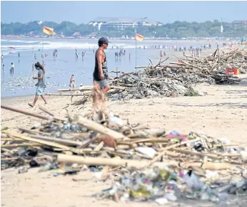  ??  ?? TROUBLE IN PARADISE: A tourist walking past debris washed up on Kuta beach near Denpasar, Bali. Indonesia is facing a plastic waste crisis driven by years of rapid economic growth.