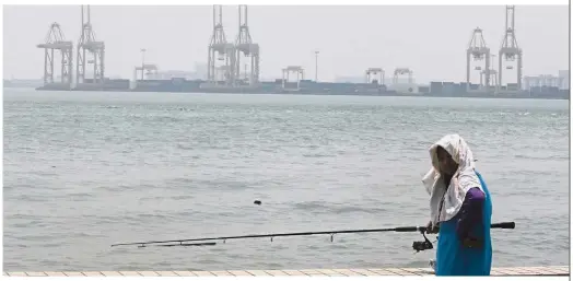  ??  ?? Searing heat and haze: An angler fishing under the hot sun at the Esplanade with the North Butterwort­h Container Terminal shrouded in haze. — ZHAFARAN NASIB/ The Star