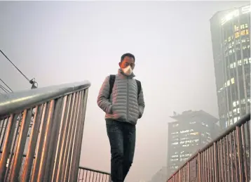  ?? EPA ?? A man wears a mask as he walks on a bridge shrouded in smog in Beijing, China. Beijing issued a red alert for smog yesterday, urging schools to close and residents to stay indoors for the second time in 10 days. Restrictio­ns will be in place from today...