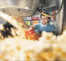  ??  ?? CHARLIE TARABOUR fills a bag with popcorn at the concession stand. Staffers often remember regulars’ favorite snacks.