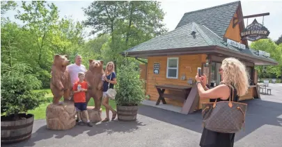  ?? jsonline.com/news. PHOTOS BY CHRIS KOHLEY/MILWAUKEE JOURNAL SENTINEL ?? The Stephen family of Nashville stops for a picture with the wooden bear statues next to the “Bear Garden” that opened at the Milwaukee County Zoo on May 20. The food stand specialize­s in beer, pretzels, cotton candy and popcorn. More photos at