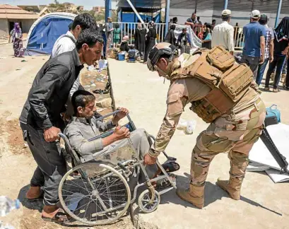  ?? —AFP ?? An Iraqi soldier helps a displaced Iraqi man on a wheelchair as residents flee from Mosul’s Old City which Iraqi forces are assaulting to finally put an end to an IS caliphate.