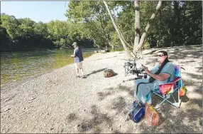  ?? NWA Democrat-Gazette/FLIP PUTTHOFF ?? Rene Hager of Fayettevil­le has it made in the shade on July 1 while she and her husband, Dave Hager, fish for trout near the cold water of the White River below Beaver Dam. The water temperatur­e in the river is around 55 degrees in the heat of summer and most of the year.