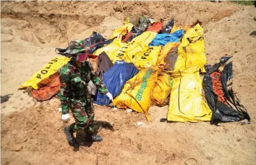  ?? Associated Press ?? ■ An Indonesian soldier walks past the bodies of tsunami and earthquake victims for a mass burial Tuesday in Palu, Central Sulawesi, Indonesia. Desperatio­n was visible everywhere Tuesday among victims receiving little aid in areas heavily damaged by a massive earthquake and tsunami, four days after the disaster devastated parts of Indonesia's central Sulawesi island.