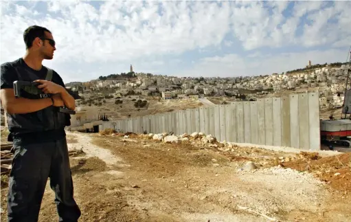  ?? PICTURE: REUTERS ?? TROUBLED: An Israeli security guard observes the controvers­ial concrete security wall, a measure Israel contends is necessary to stop suicide bombers and which Palestinia­ns condemn as a land grab, on the outskirts of Jerusalem.