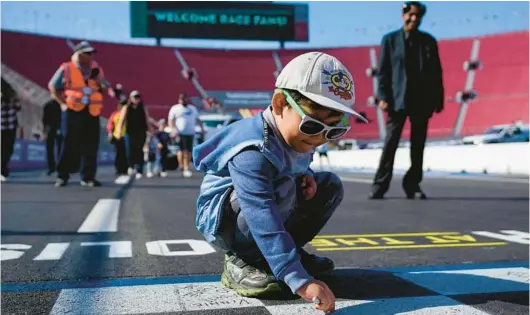  ?? ASHLEY LANDIS/AP ?? A young fan signs his name on the finish line ahead of NASCAR practice sessions Saturday at the Los Angeles Memorial Coliseum.