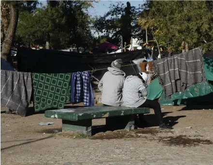  ?? AP FILE ?? HALTED: A migrant fleeing gang violence in his home region outside Guadalajar­a, Mexico, sits with his son on a bench in Juarez. The family has been living in the tent camp for two months while waiting to apply for asylum in the United States.