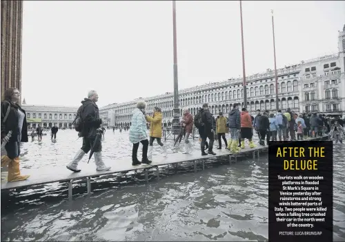  ??  ?? Tourists walk on wooden platforms in flooded St Mark’s Square in Venice yesterday after rainstorms and strong winds battered parts of Italy. Two people were killed when a falling tree crushed their car in the north west of the country.