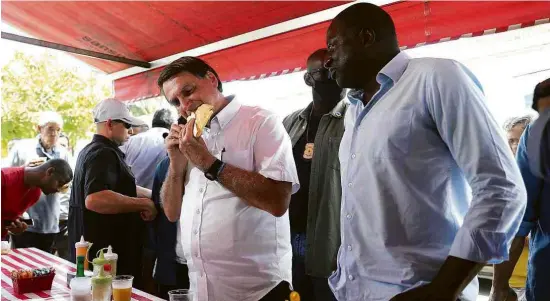  ?? Pilar Olivares/Reuters ?? O presidente Jair Bolsonaro come pastel em feira ao lado do deputado Hélio Lopes depois de votar na manhã deste domingo, no Rio