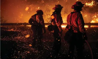  ??  ?? Firefighte­rs shield themselves as strong winds whip embers through the air from the Bond fire on 3 December. Photograph: Kent Nishimura/Los Angeles Times/REX/Shuttersto­ck