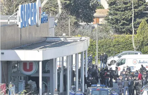  ??  ?? SELFLESS ACTION: Police gather outside the Super U supermarke­t in Trebes, southern France, where a man took hostages, killing four before he was killed by security forces.