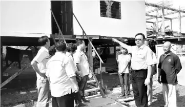  ??  ?? Lo is seen pointing to one at the houses in Dewa Wira repaired under the Poverty Eradicatio­n Programme, as local community leaders and locals look on.