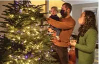  ??  ?? Ani Sirois places lights and decoration­s on the family’s Christmas tree with daughter Ida, 2, and husband Chadwick at their Portland, Oregon, home on Nov. 24. Her family opted to pick their own tree this year instead of buying a pre- cut one as usual.