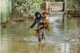  ?? Photograph: Fayaz Aziz/Reuters ?? A girl carries her sibling as she walks through stranded flood water, following rains and floods during the monsoon season in Nowshera, Pakistan, last September.