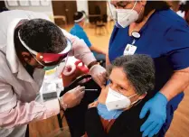  ?? STEPHEN M. KATZ/STAFF FILE ?? CVS pharmacist Kevin Gordon administer­s the COVID-19 vaccinatio­n to Ann Belton, 70, as registered nurse Nancy Rose comforts her at a vaccinatio­n clinic for staff and residents at Virginia Beach’s Beth Sholom Village in December.