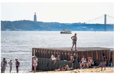  ?? — AFP ?? Keeping
cool: Tourists resting in the shade on a beach next to the Tagus River at Ribeira das Naus in Lisbon, Portugal.