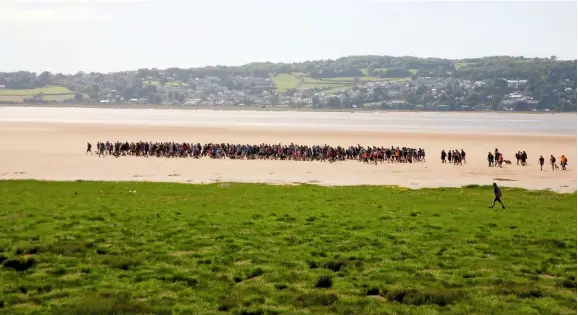  ??  ?? Walkers gather to cross from Arnside to Kents Bank, Cumbria, guided by the Queen’s guide to the sands, a position dating from the 16th century. The guide escorts visitors over the treacherou­s mudflats and tidal sands of Morecambe Bay for a nominal salary of £15 a year and the use of a cottage. Fisherman Michael Wilson took on the role in 2019.