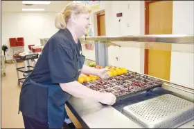  ?? (NWA Democrat-Gazette/Rachel Dickerson) ?? Food service worker Janelle Davison stocks trays of fruit at the Cooper Elementary School cafeteria before lunch begins on March 8. Cooper Elementary, Pea Ridge Schools and Gravette Schools recently received funds to relieve lunch debt. The funds were raised by St. Theodore’s Episcopal Church in Bella Vista and the Bella Vista Recycling Center.