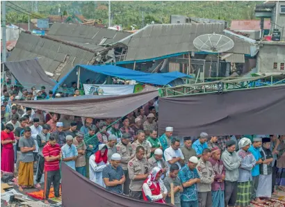  ?? AP ?? faithful offer prayers as houses ruined by sunday’s earthquake are seen in the background at a makeshift mosque in Pamenang, Lombok island, indonesia, on friday. the north of the popular resort island has been devastated by the earthquake that damaged thousands of buildings and killing a large number of people. —