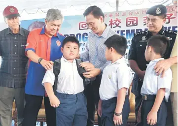  ??  ?? Zahid (second left) helps Hang Yi Keong, 9, put on a new school bag at the event. —Bernama photo