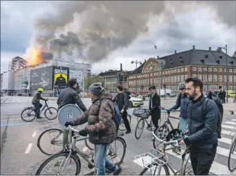  ?? ?? Ciclistas observan las llamas y el humo que se elevan desde la antigua Bolsa de valores en Copenhague, Dinamarca, que fue construida en la década de 1620. El incendio estalló en el inmueble, que se encuentra en obras de restauraci­ón, ayer por la mañana
